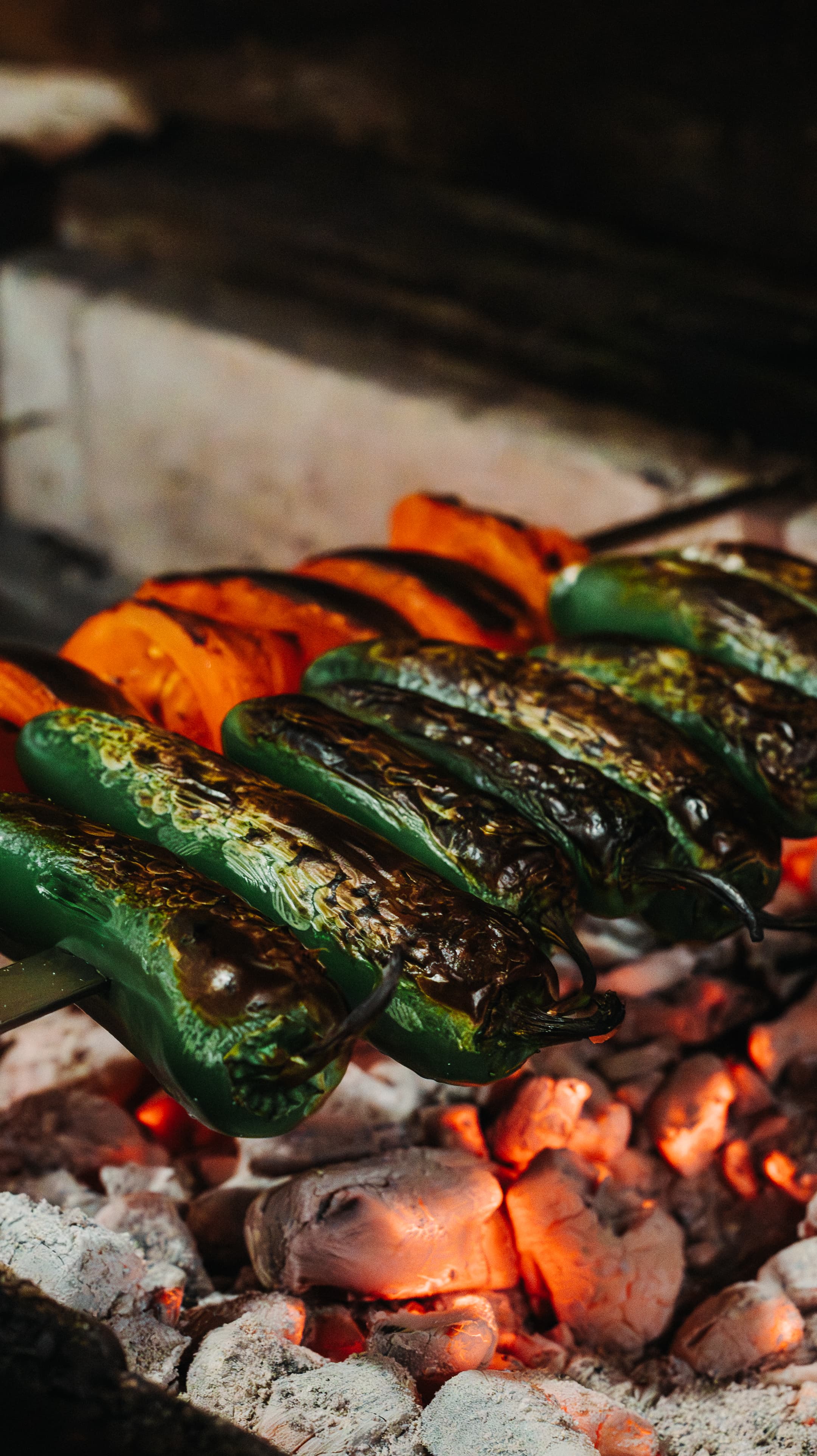 Grilled peppers and tomatoes side by side on the coals