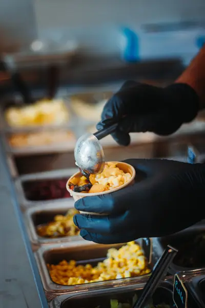 Black-gloved hands scooping corn into a takeaway