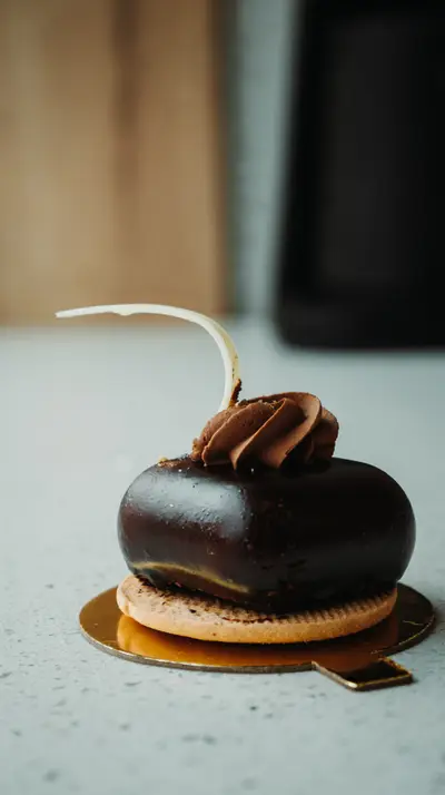 A dark-glazed entremet topped with a chocolate rosette and a sugar curl