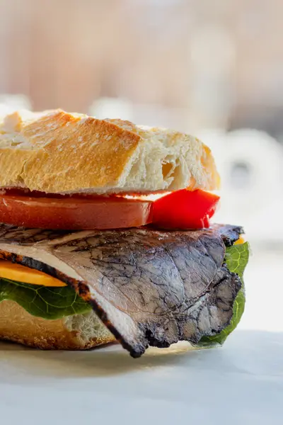 A sandwich of sliced meat, tomato and cheese in a ciabatta roll