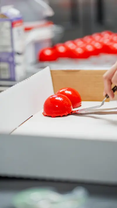 A gloved hand lifting a red-glazed dome with a palette knife