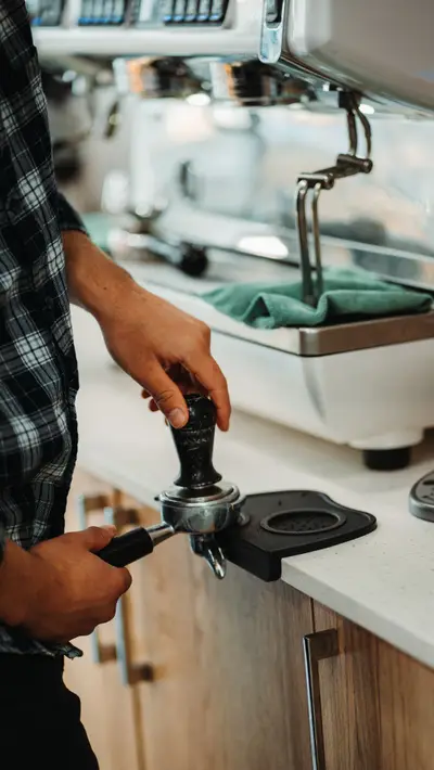 A barista holding the portafilter at the espresso machine