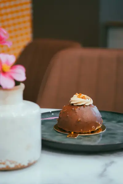 A glazed dome cake on a plate beside a vase with a pink flower
