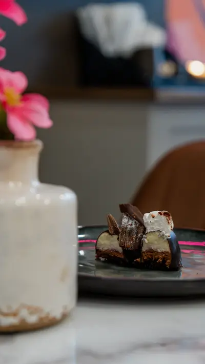 A layered chocolate slice on a plate beside a vase