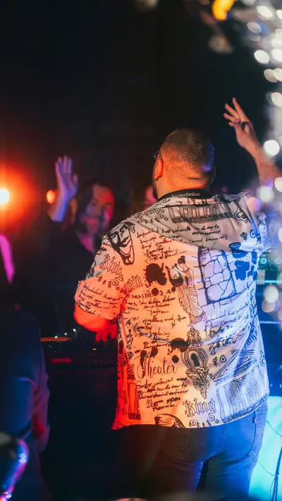 A DJ with arms raised behind the decks under club lighting