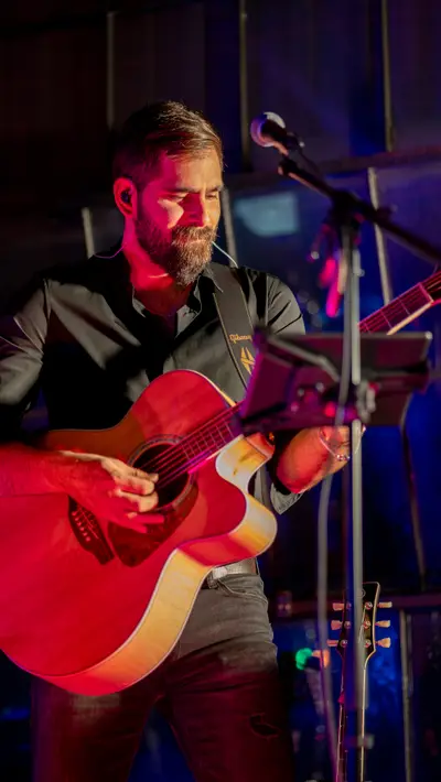 A guitarist playing a red acoustic guitar on stage