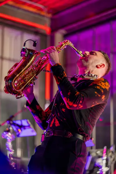 A saxophonist mid-phrase under magenta light