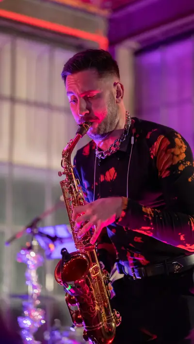 A saxophonist in a patterned shirt washed in red light