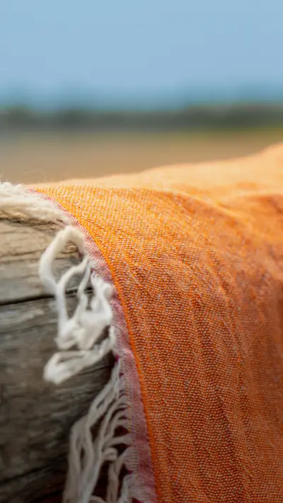 An orange fringed towel over a driftwood rail