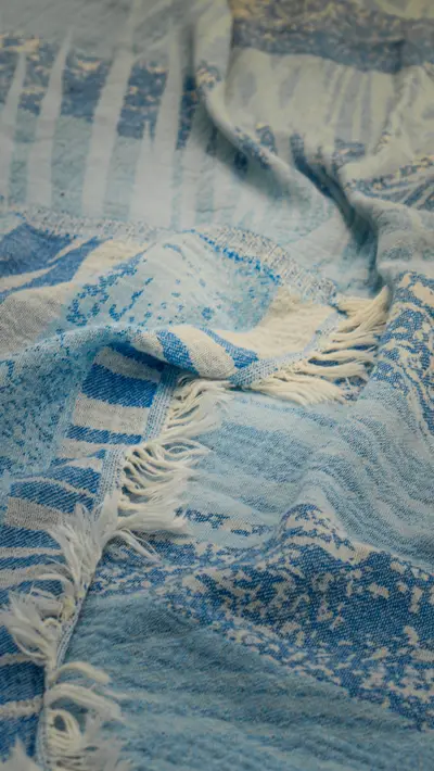 A blue and white towel with its fringe spread on sand