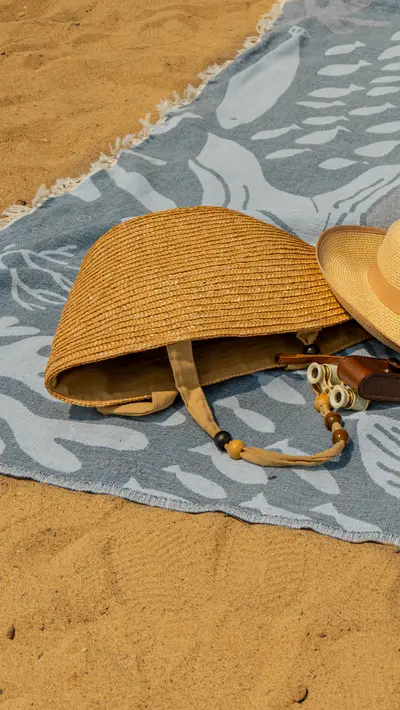 A straw bag and hat resting on a pale blue towel