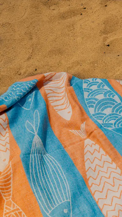 A fish-printed towel spread open on the beach