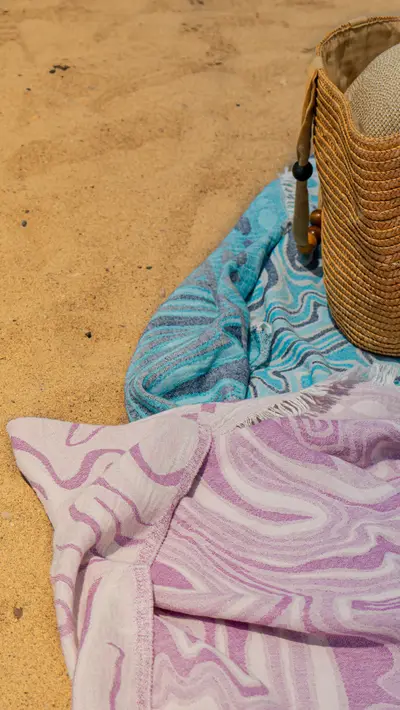 A lilac marbled towel beside a woven bag