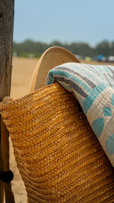 A straw bag and towel leaning against a wooden post