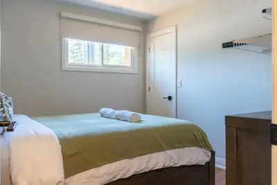 A made bed with folded towels and a window above