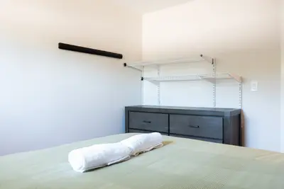 A bed with folded towels facing a dresser and hanging rail