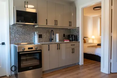 A kitchen with oven and microwave, bedroom through the doorway
