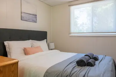 A bed with a grey throw and rolled towels beneath the window