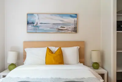 A bed beneath a framed sailing picture with ochre cushion