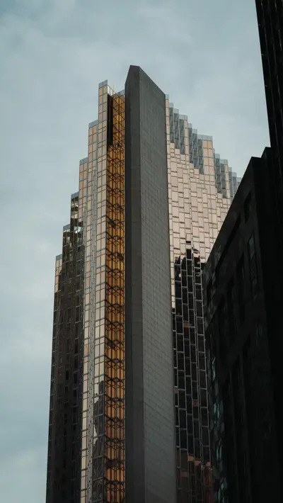 A tower rising between darker buildings against cloud