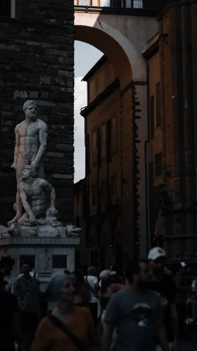 A statue above a crowd moving through the piazza