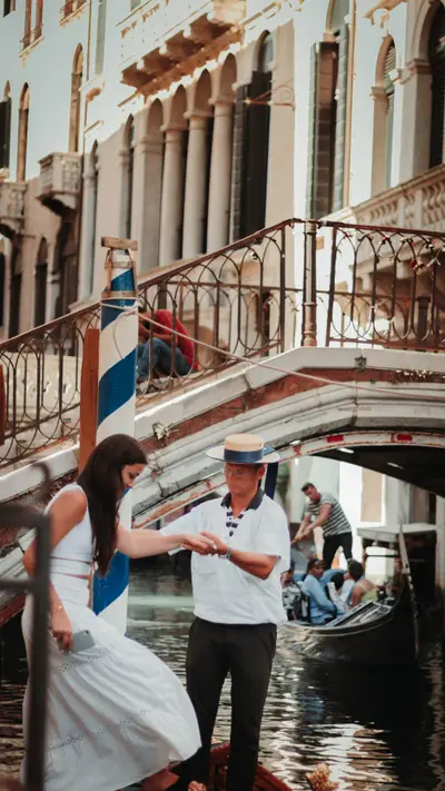 A gondolier helping a passenger ashore beneath a bridge