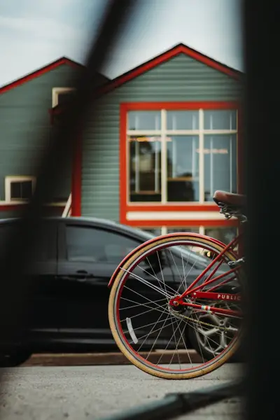 A red bicycle parked beside a car in front of a clapboard house