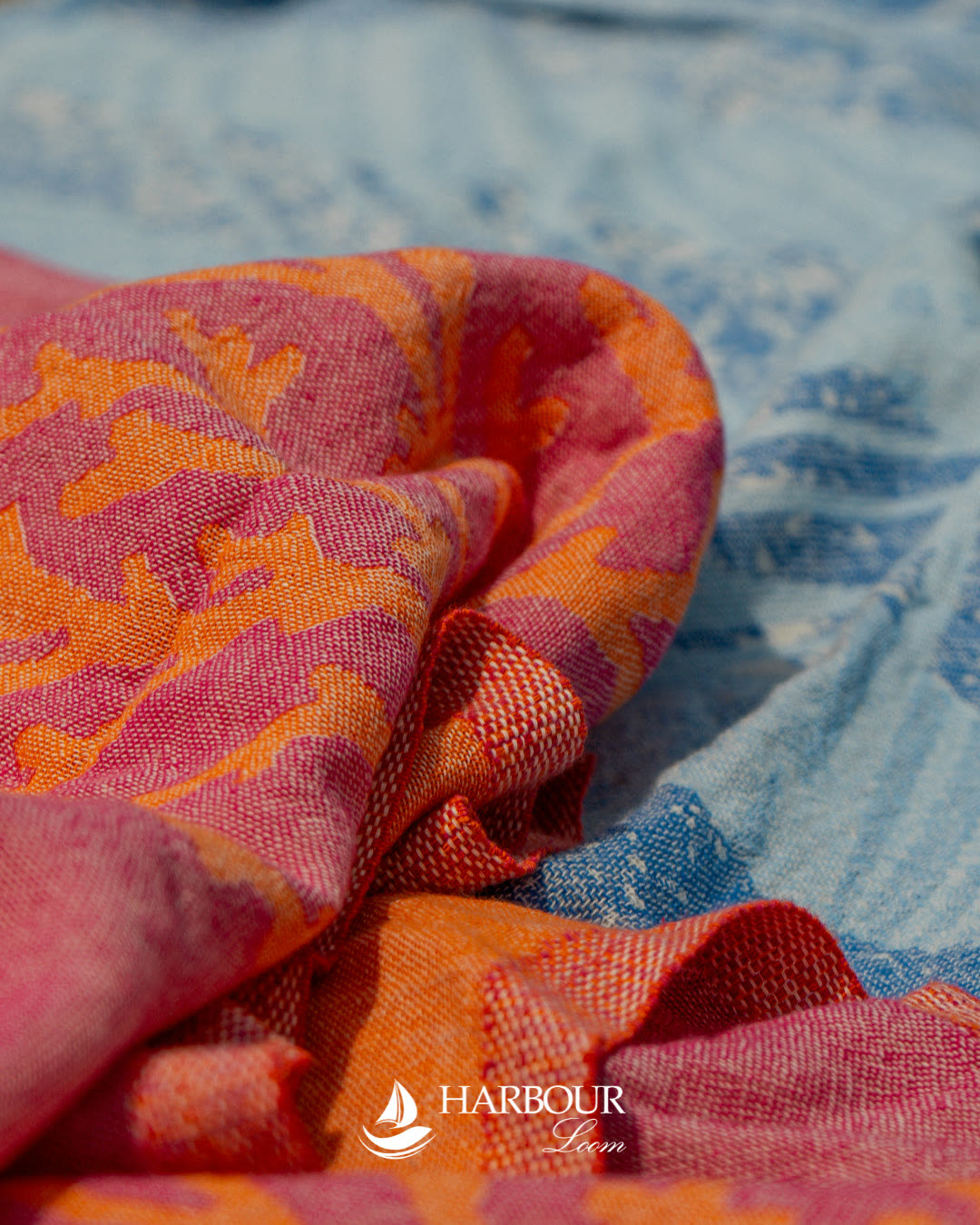 Macro photograph of a pink and orange patterned Harbour Loom weave folded over a blue cloth