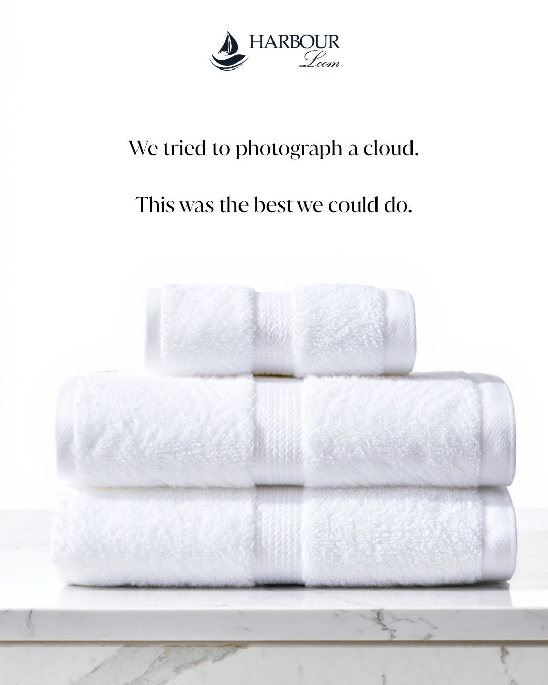 Three folded white hotel towels stacked on a marble counter against a pure white background